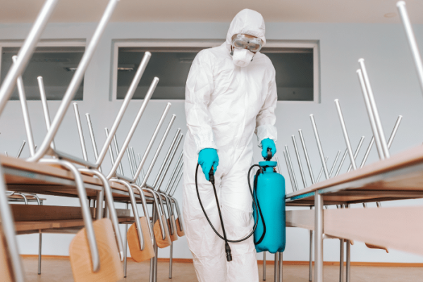 40aff4d5-man-sterile-uniform-with-gloves-mask-holding-sprayer-spraying-with-disinfectant-floor-classroom-1.png